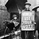 An American suffragette with an umbrella stands next to a baby carriage and wears a sign proclaiming ‘Women! Use your vote,’ circa 1920.